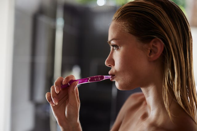 Profile view of young woman brushing her teeth during morning routine in bathroom.
