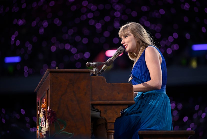 Taylor Swift playing the piano at the Eras Tour in a blue dress.
