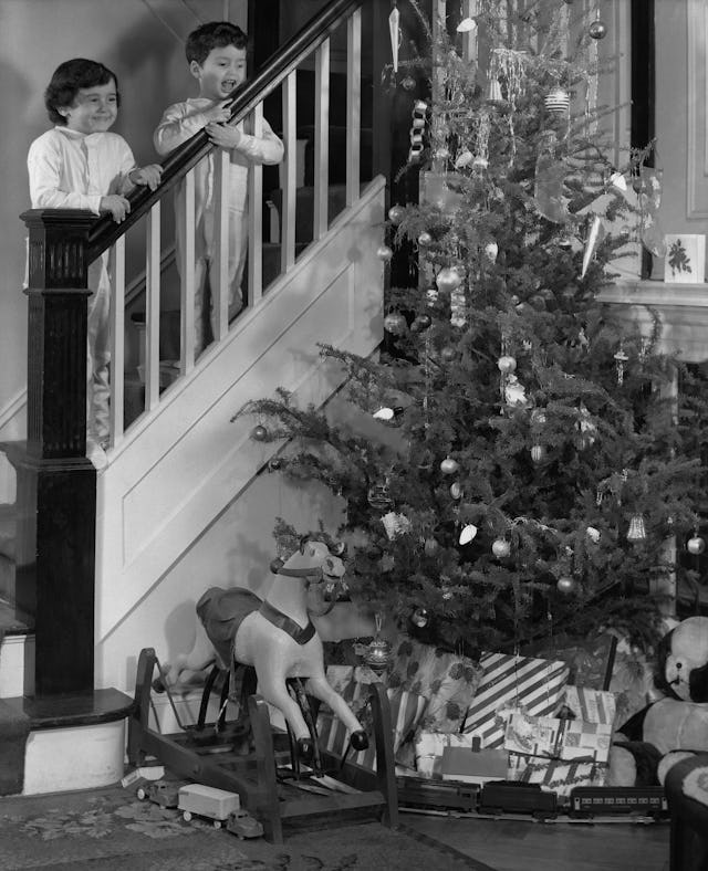 Young boy and his sister in pajamas standing on the staircase at the railing looking down on a Chris...
