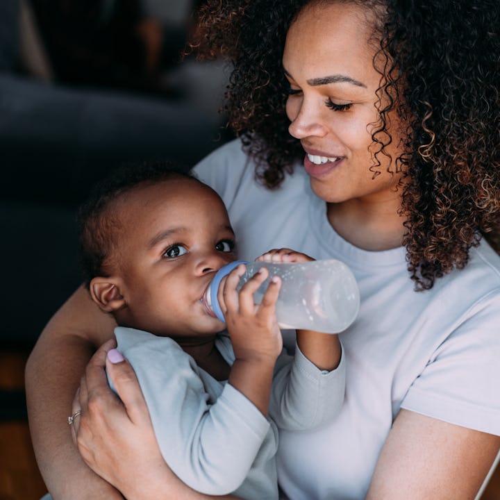 Portrait of a happy African-American woman holding and feeding her cute baby boy and enjoying mother...