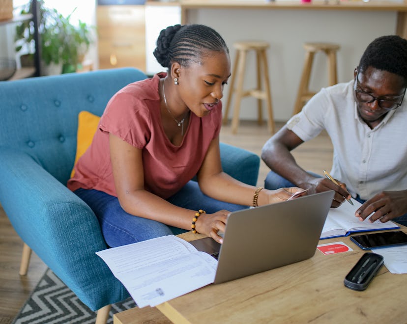 Young black married couple looking at computer screen, analyzing household budget, paying bills in e...
