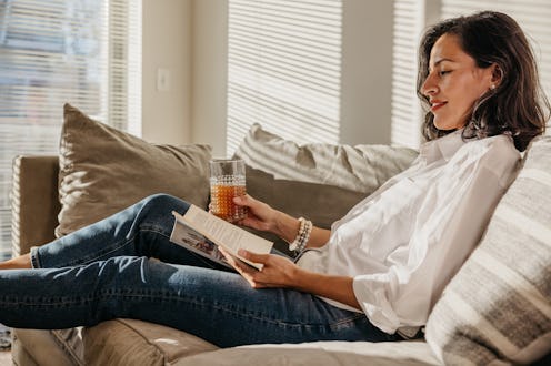 Woman enjoying a day off and reading a book on the couch in their home in New York.