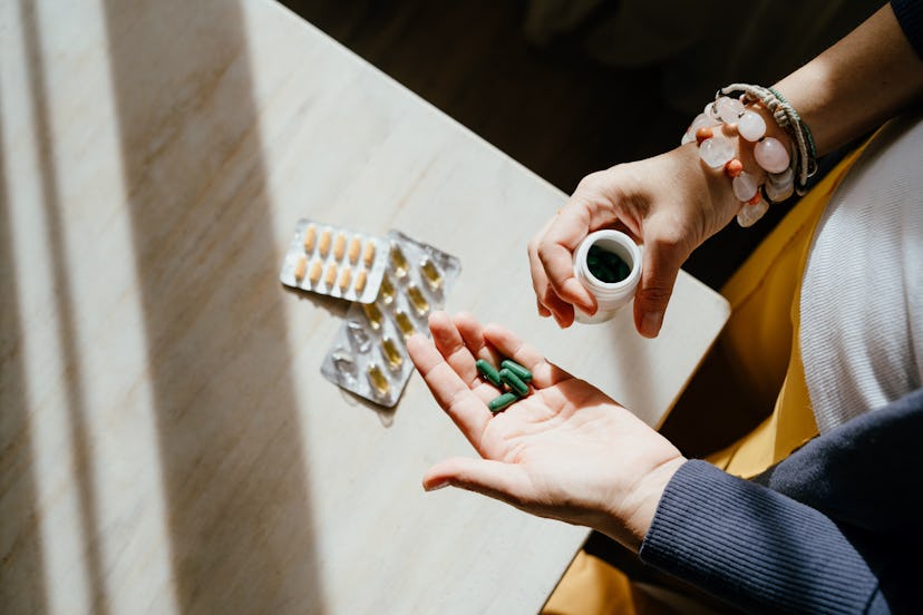 Mature woman standing at a table with green pills in her hand. Taking vitamins, macro elements and b...