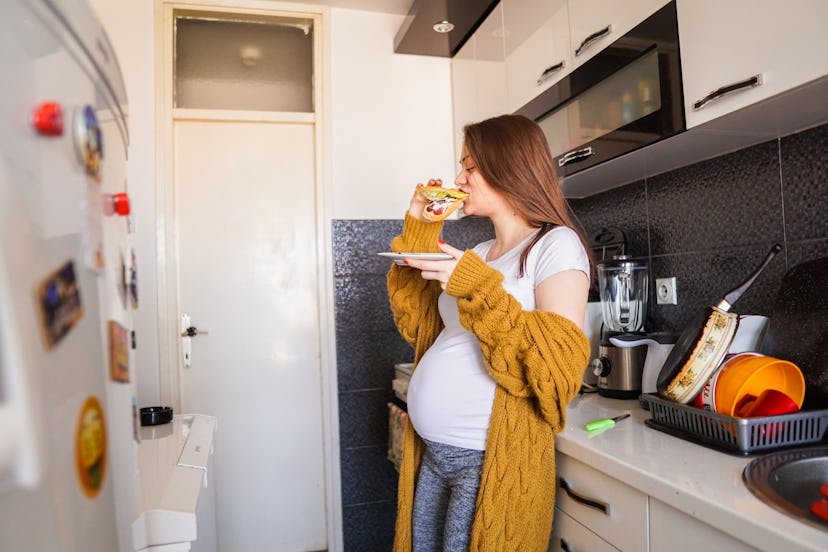 Pregnant woman eating sandwich in her kitchen, in a story about what to eat before one-hour glucose ...