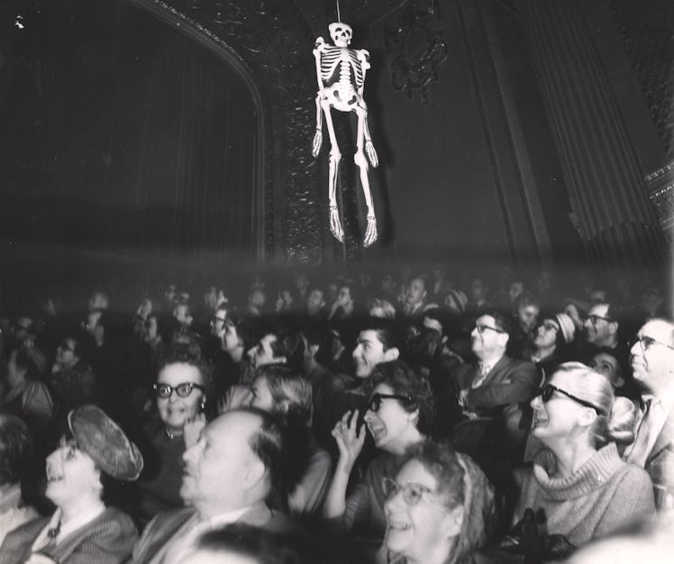 An audience laughs as an inflatable skeleton hangs over their heads, late 1950s or early 1960s. They...