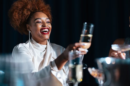 Happy African-American woman toasting with alcohol and having fun with her unrecognizable multi-ethn...