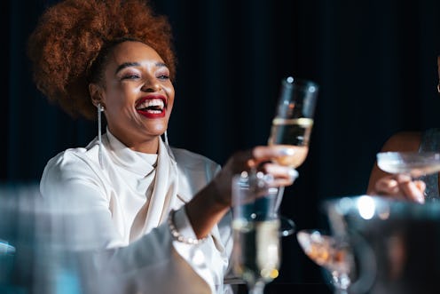 Happy African-American woman toasting with alcohol and having fun with her unrecognizable multi-ethn...