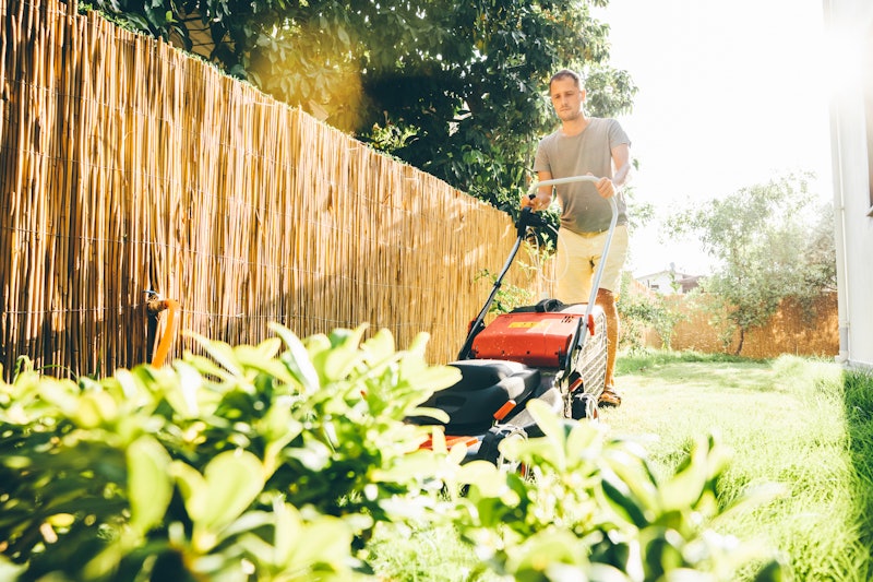 Man using a lawn mower in his back yard.