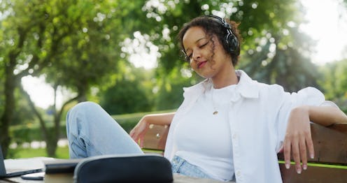 A young woman taking a break from studying in the park. She is listening to music to regain some new...