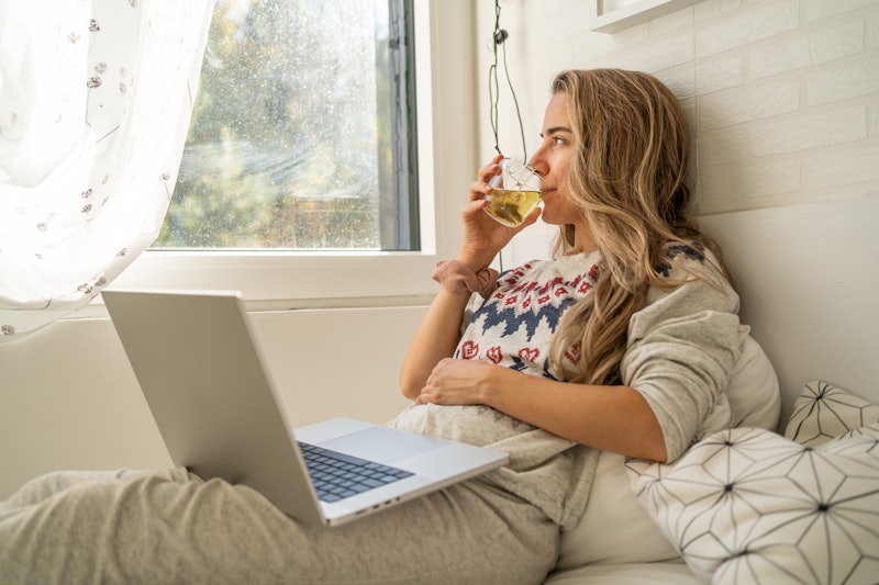A woman is using a laptop in bed during a beautiful morning