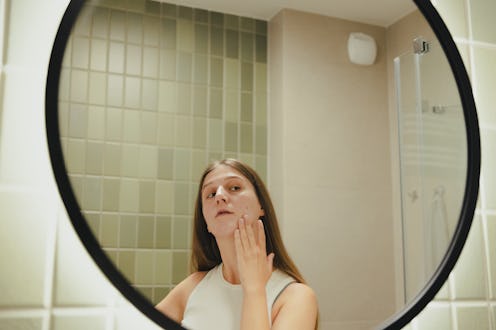 Female with long hair doing beauty routine in the modern bathroom applying beauty product on her irr...