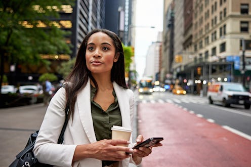 Waist up view of longhaired Black professional in office attire standing curbside, bag on shoulder, ...