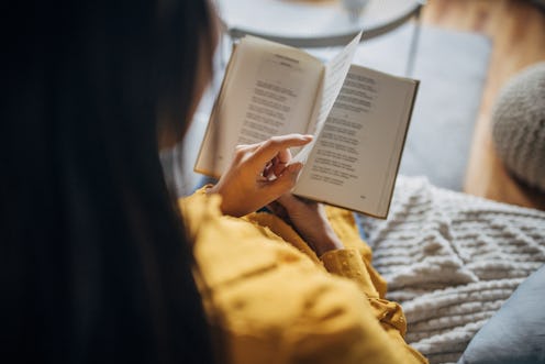 Over the shoulder view of a young Japanese woman reading a book on the sofa.