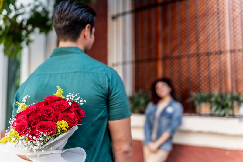 Mid adult man holding bouquet of flowers behind his back to surprise his girlfriend outdoors - Valen...