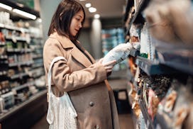 Young Asian pregnant woman carrying a reusable shopping bag and choosing healthy snacks from product...