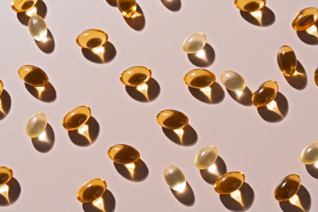 Gold Colored Soft Gel Capsules on Beige Background High Angle View.