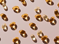 Gold Colored Soft Gel Capsules on Beige Background High Angle View.