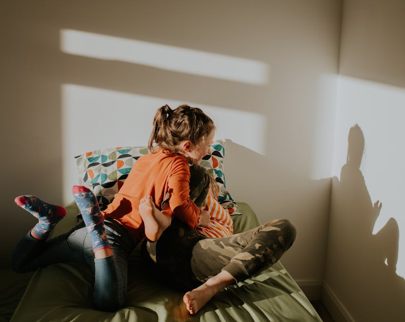 A sister pins her brother to the bed as they wrestle and playfully fight.