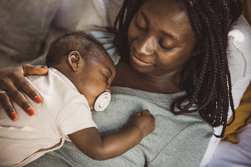Young mother taking care of her baby son. She is holding baby while he is at sleep.
