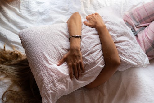 An unrecognizable woman covers her face with a pillow while lying on the bed