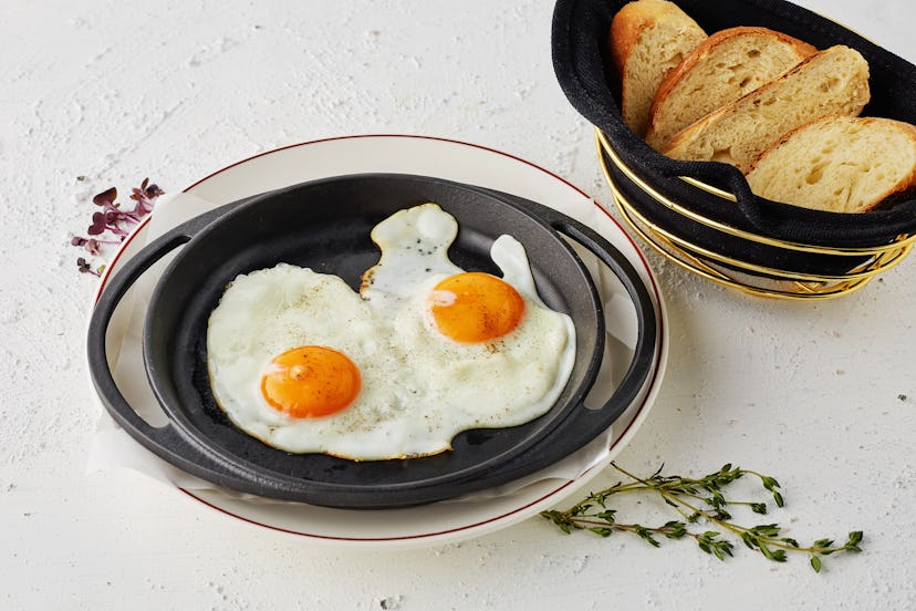 Sunny side up eggs served in griddle pan with slice of breads for breakfast, on white background wit...