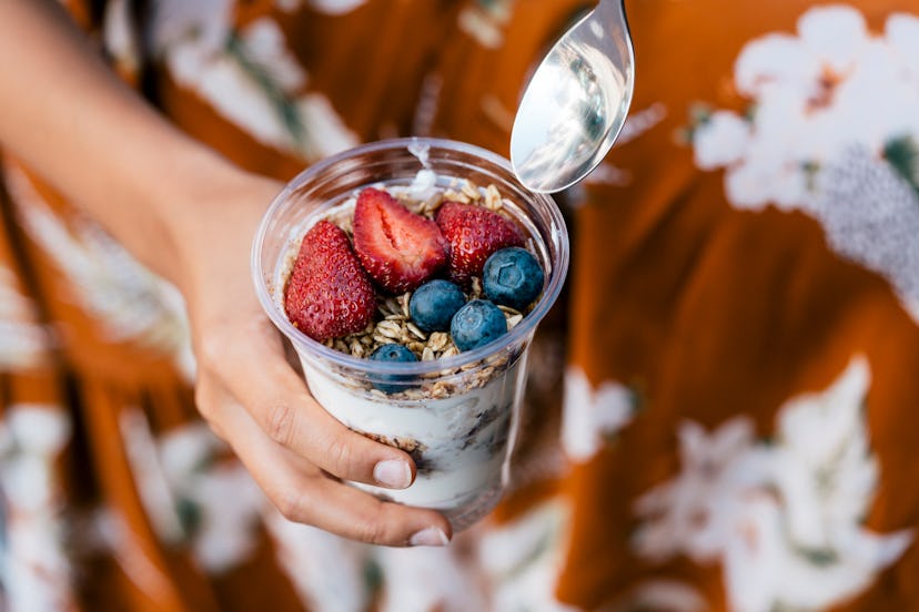 Bowl of yogurt with berries and oatmeal, woman holding in hand, ready to eat