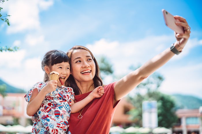 Young pretty mom & her lovely daughter taking selfie with smartphone while enjoying ice cream during...