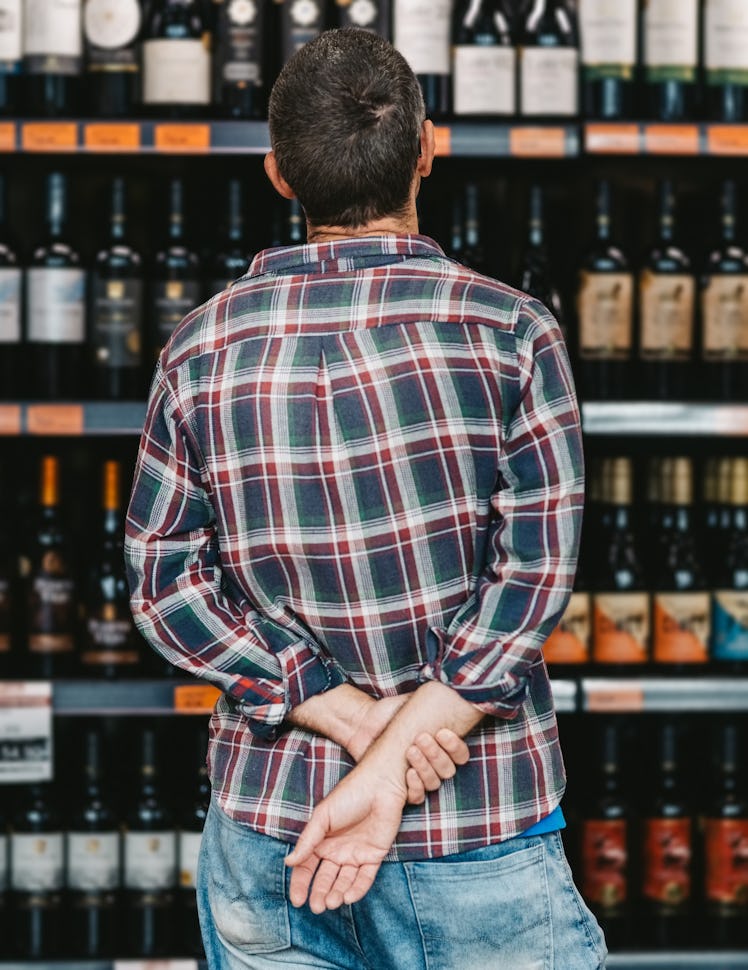 Rear view of a male customer looking at a rack of wine in supermarket