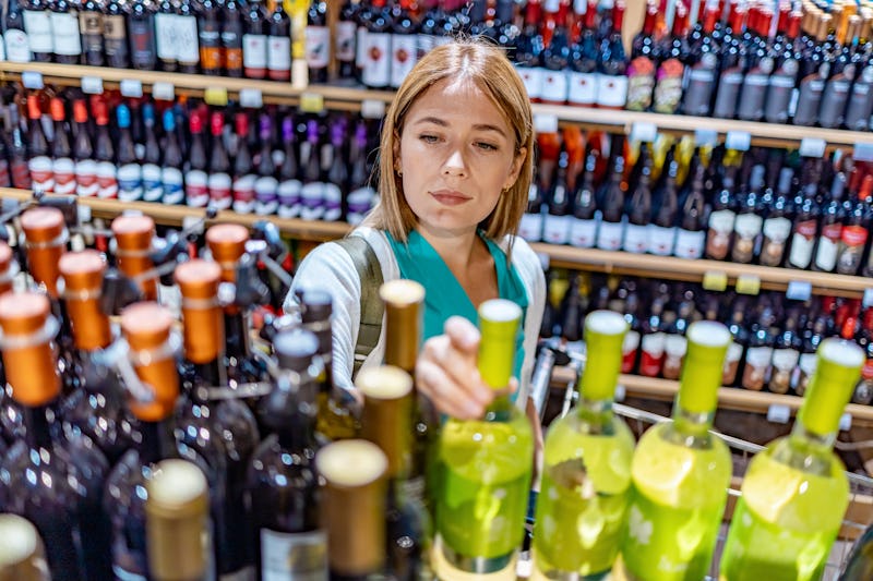 Woman deciding what wine to buy and shopping in supermarket