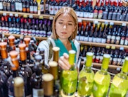 Woman deciding what wine to buy and shopping in supermarket