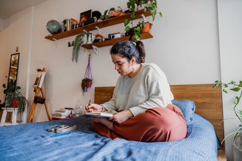 Young woman sitting on the bed drawing in notepad in the bedroom