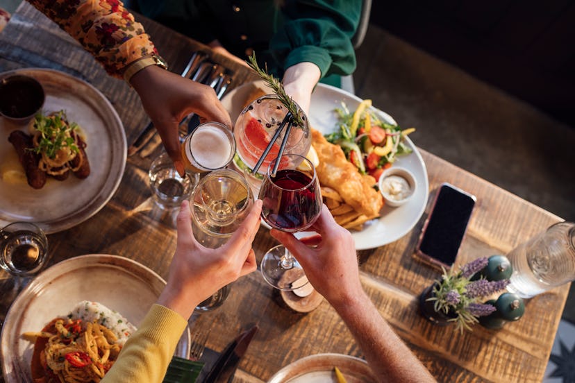 Overhead view of four unrecognizable friends cheering their glasses together over the ir freshly pre...