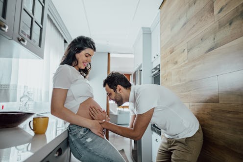 Mid adult man talking to pregnant woman's belly in the kitchen at home