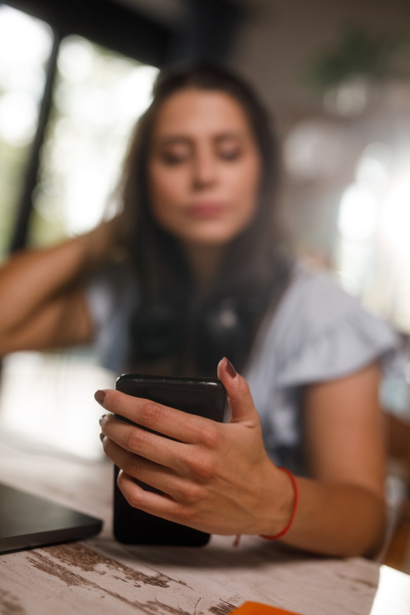 Selective focus shot of bored young woman checking notifications and text messages on her smart phon...