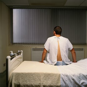 A man in a hospital gown sitting on a hospital bed.