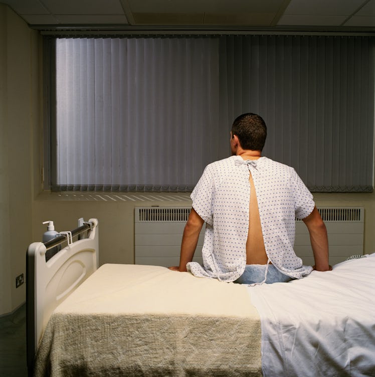 A man in a hospital gown sitting on a hospital bed.