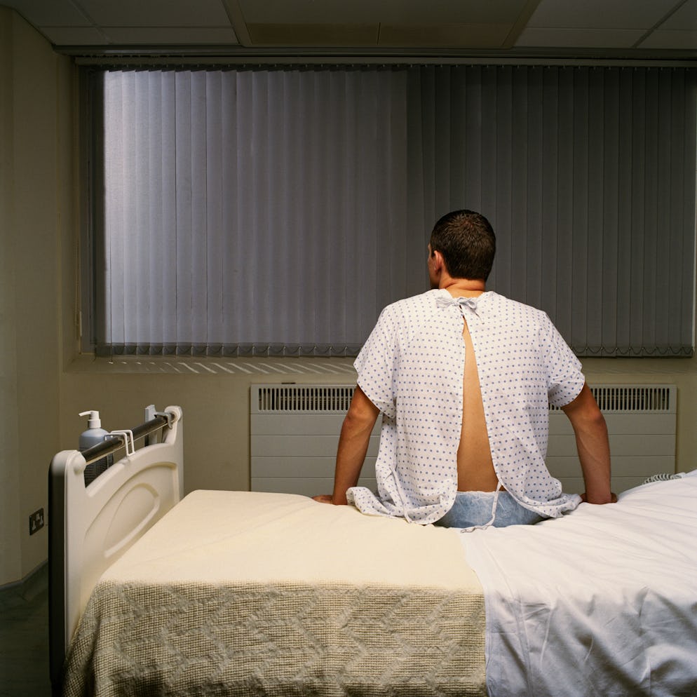 A man in a hospital gown sitting on a hospital bed.
