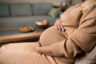 Close-up of unrecognizable pregnant woman touching her belly while sitting at home