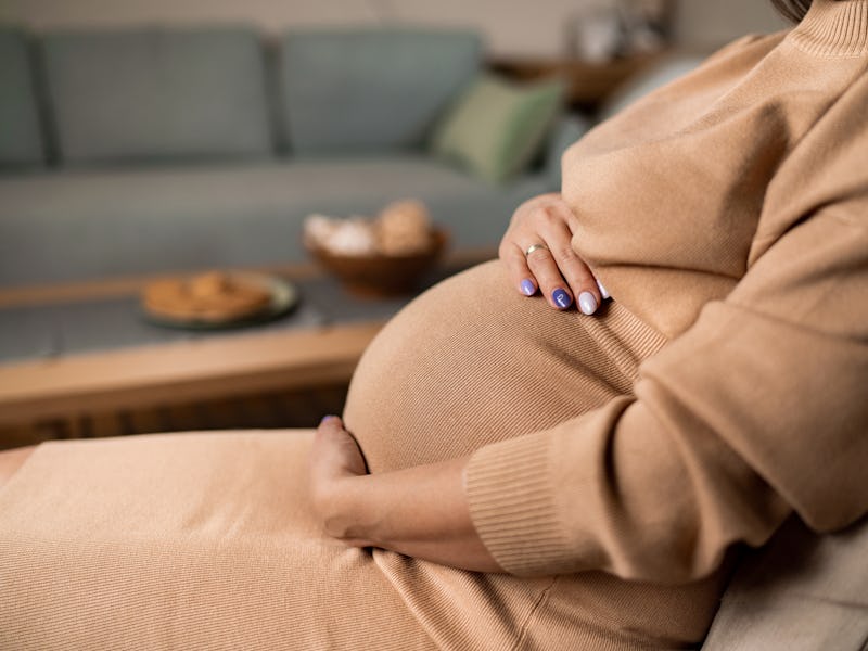 Close-up of unrecognizable pregnant woman touching her belly while sitting at home