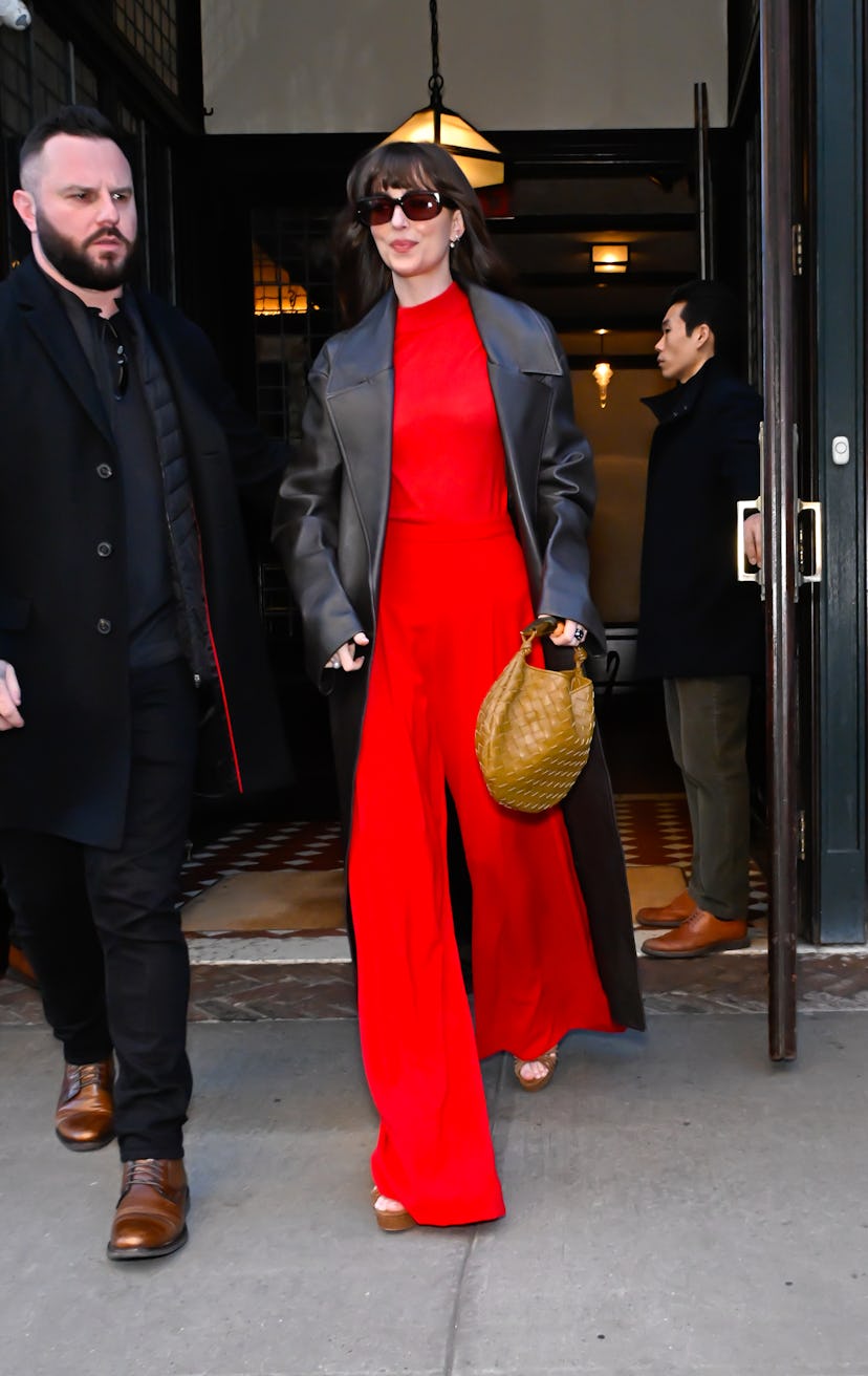 Dakota Johnson wears a red jumpsuit and leather trench in soho on February 07, 2024 in New York City...