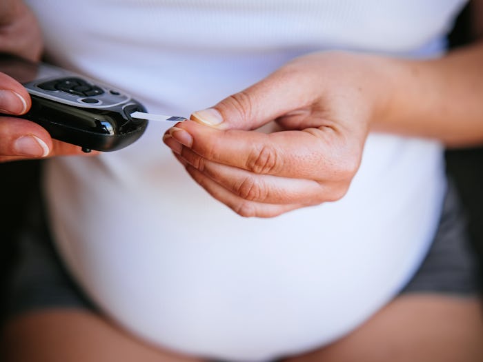Pregnant woman is using a glucometer at home.