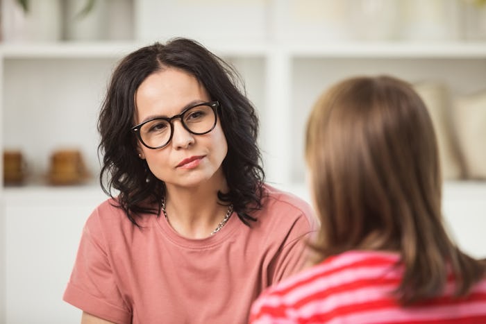 Worried mature woman sitting on sofa in the living room at home and listening to teenage girl. They ...