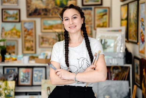 Portrait of a Talented Young Female Artist With Arms Crossed Holding Brushes in her Creative Art Stu...