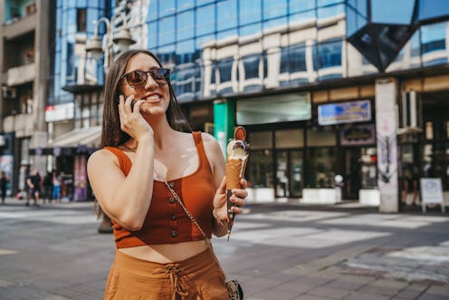 Beautiful young woman talking on mobile phone while eating ice cream in the city on sunny summer day