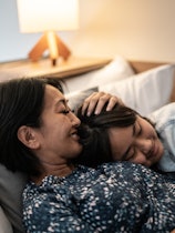 Mother laying down with daughter in bed at home