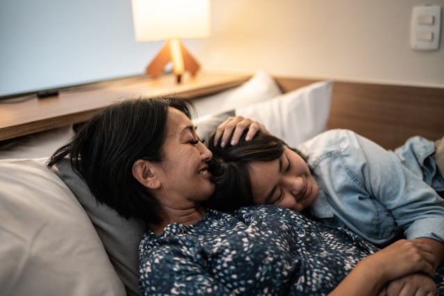 Mother laying down with daughter in bed at home