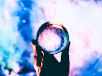 Hand holding a crystal ball with a mesmerizing swirl of cosmic colors inside, creating a portal-like...