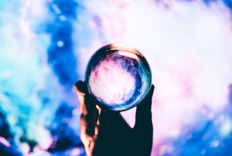 Hand holding a crystal ball with a mesmerizing swirl of cosmic colors inside, creating a portal-like...