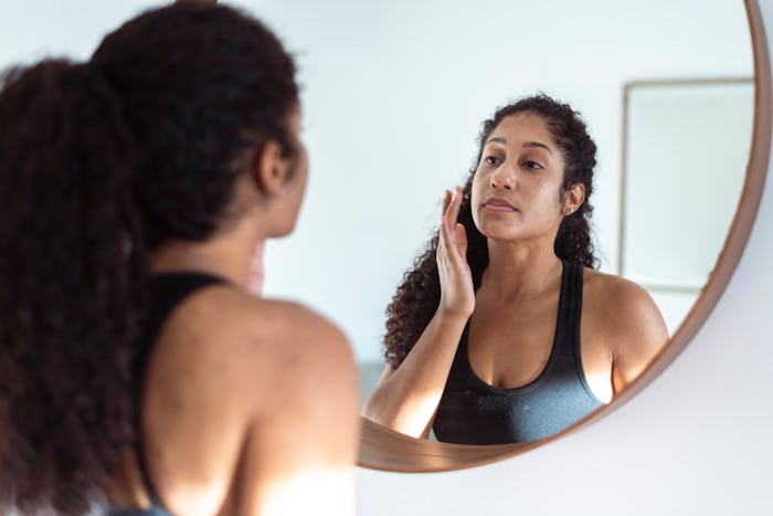 Woman applies moisturizer in mirror, in a story explaining why some people get acne after weaning fr...