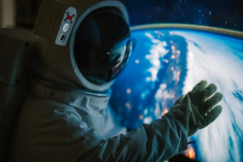 Asian chinese mid adult female astronaut looking at earth through window from spaceship at outer spa...